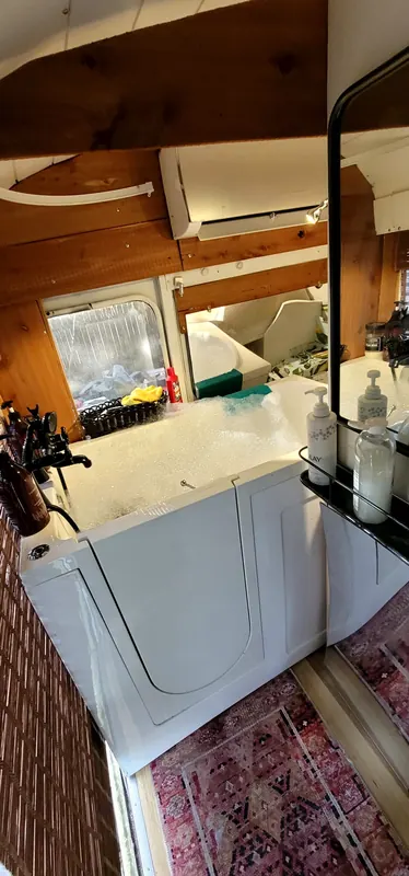 Walk-in soaking tub full of bubbles inside the Camp Calypso bus, with a wood ceiling and mini-split AC