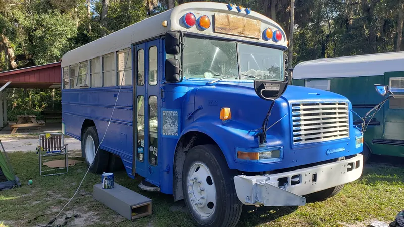 A school bus mid paint job in bright blue with fresh white bumpers
