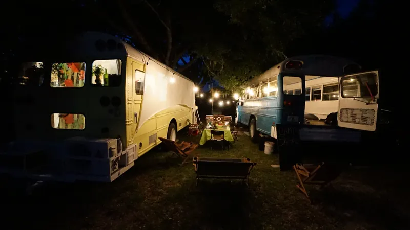 Two skoolies at night with string lights over a camp dinner table